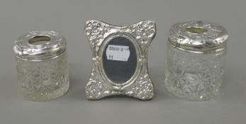 A small silver frame and two silver topped hair tidies. The former 7.5 cm wide.