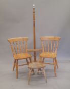 An Ercol elm seated child's chair, two pine kitchen chairs and a standard lamp.