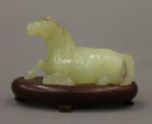 A green jade model of a recumbent horse, on a wooden base. 6.5 cm high overall.