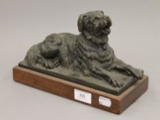 A bronze model of a recumbent dog on a wooden plinth base. 26.5 cm long.