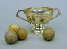 A silver golf trophy cup and four golf balls. The cup 9 cm high. The cup 171.1 grammes.
