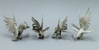 Four white metal models of cockerels. The largest 18 cm high.