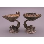 A small pair of Continental unmarked cast silver dolphin table salts, supporting shell bowls.