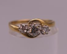 An 18 ct gold three stone diamond crossover ring. Ring size K. 2.7 grammes total weight.