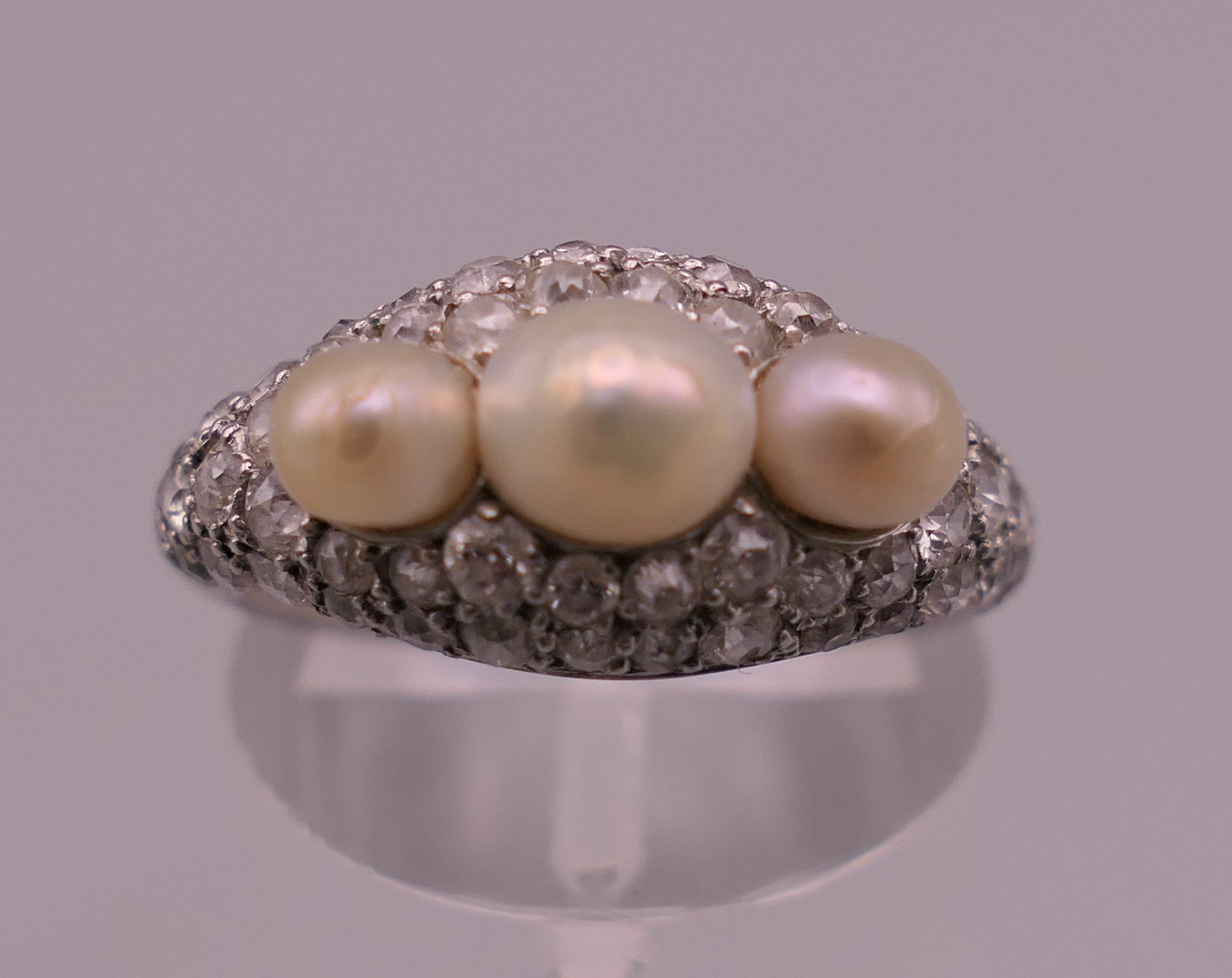 An unmarked white gold or platinum diamond and pearl ring. Ring size I/J. 5.6 grammes total weight.