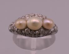 An unmarked white gold or platinum diamond and pearl ring. Ring size I/J. 5.6 grammes total weight.