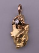 An unmarked gold (probably 18 ct) nugget pendant set with a diamond, on a 9 ct gold suspension loop.