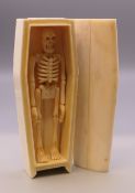 A bone model of a skeleton in coffin. 11.5 cm long overall.