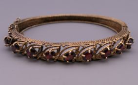 A 14 ct gold garnet bangle form bracelet. 6.5 cm wide. 22 grammes total weight.