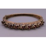 A 14 ct gold garnet bangle form bracelet. 6.5 cm wide. 22 grammes total weight.