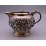 An Indian unmarked silver cream jug with elephant head handle, relief decorated with deities.