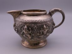 An Indian unmarked silver cream jug with elephant head handle, relief decorated with deities.