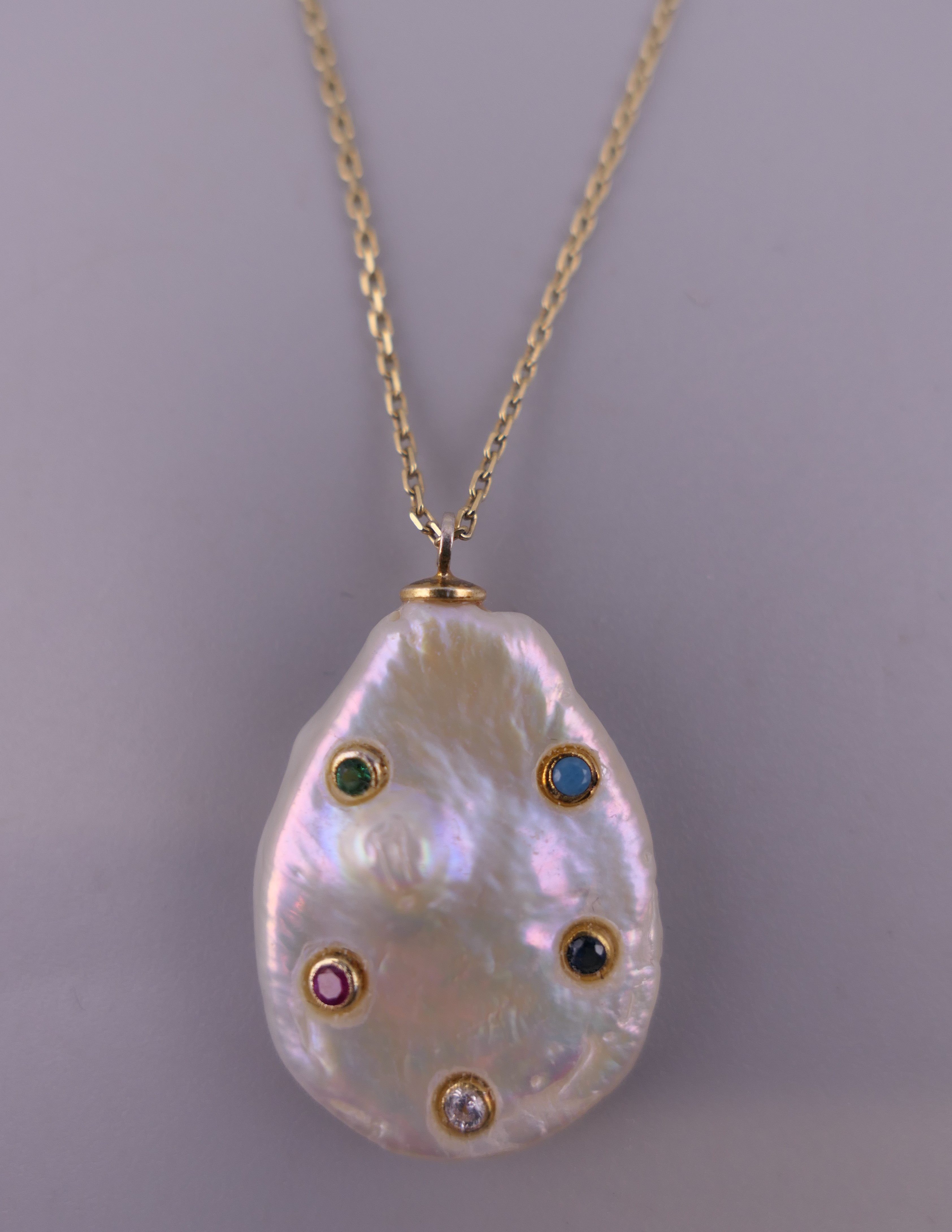 A stone set mother-of-pearl pendant mounted on a silver gilt chain. The pendant 2.5 cm high.