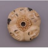 A bone toggle carved with faces. 4 cm diameter.