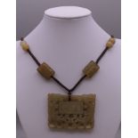 A jade pendant on cord decorated with calligraphy. The pendant 6 cm wide.