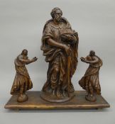 A 17th century carved group of a Saint and two Acolytes, mounted on a plinth base. 56 cm high.