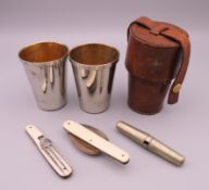 A pair of leather cased cups, a folding spoon and fork, and a corkscrew. Cups 7 cm high.