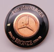 A Mercedes 'Everyday Heroes 2004/05 Bronze' lapel pin. 2.5 cm diameter.