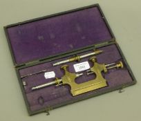 A cased antique brass clock maker's tool. The case 27.5 cm long.