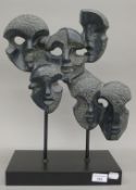 An African carved stone multi mask sculpture, on display stand. 45 cm high.