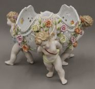 A Continental porcelain bowl supported by three cherubs. 23 cm high.