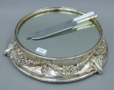 A silver plated cake stand with mirrored top, together with two cake knives.