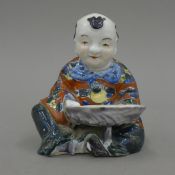 A Chinese brush washer in the form of a seated boy holding a shell. 12 cm high.