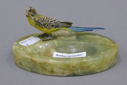 An onyx ash tray surmounted with a cold painted model of a budgerigar. 12 cm wide.