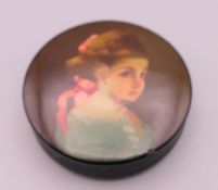 A papier mache snuff box depicting a young girl. 6 cm diameter.