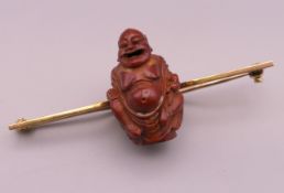 An unmarked gold brooch, set with a carved model of Buddha. 5.75 cm long, Buddha 2.5 cm high.