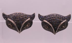 A pair of diamond and sapphire cat mask form earrings. 3 cm wide.