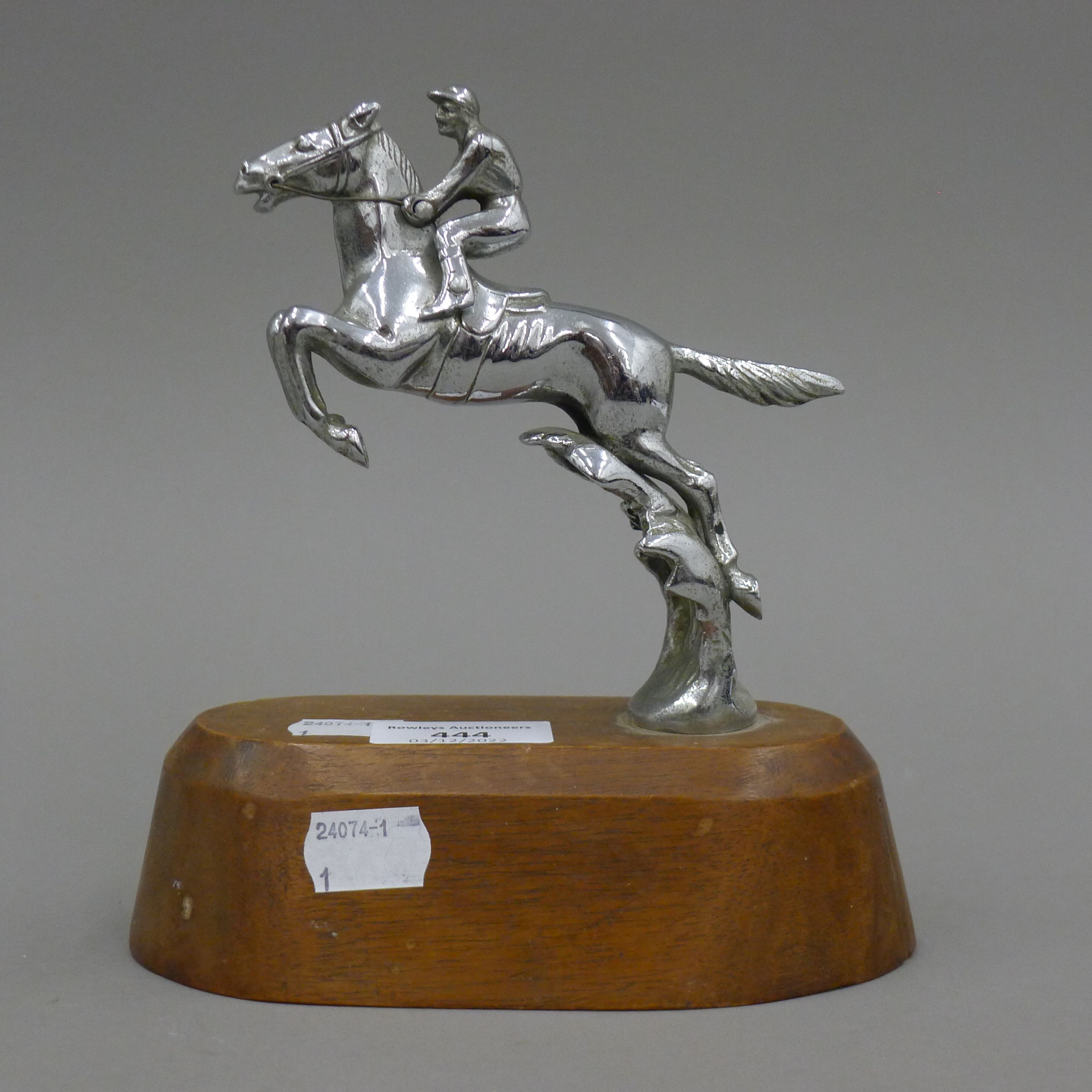 A mid-20th century car mascot formed as a leaping horse and jockey, mounted on a wooden stand. 17.