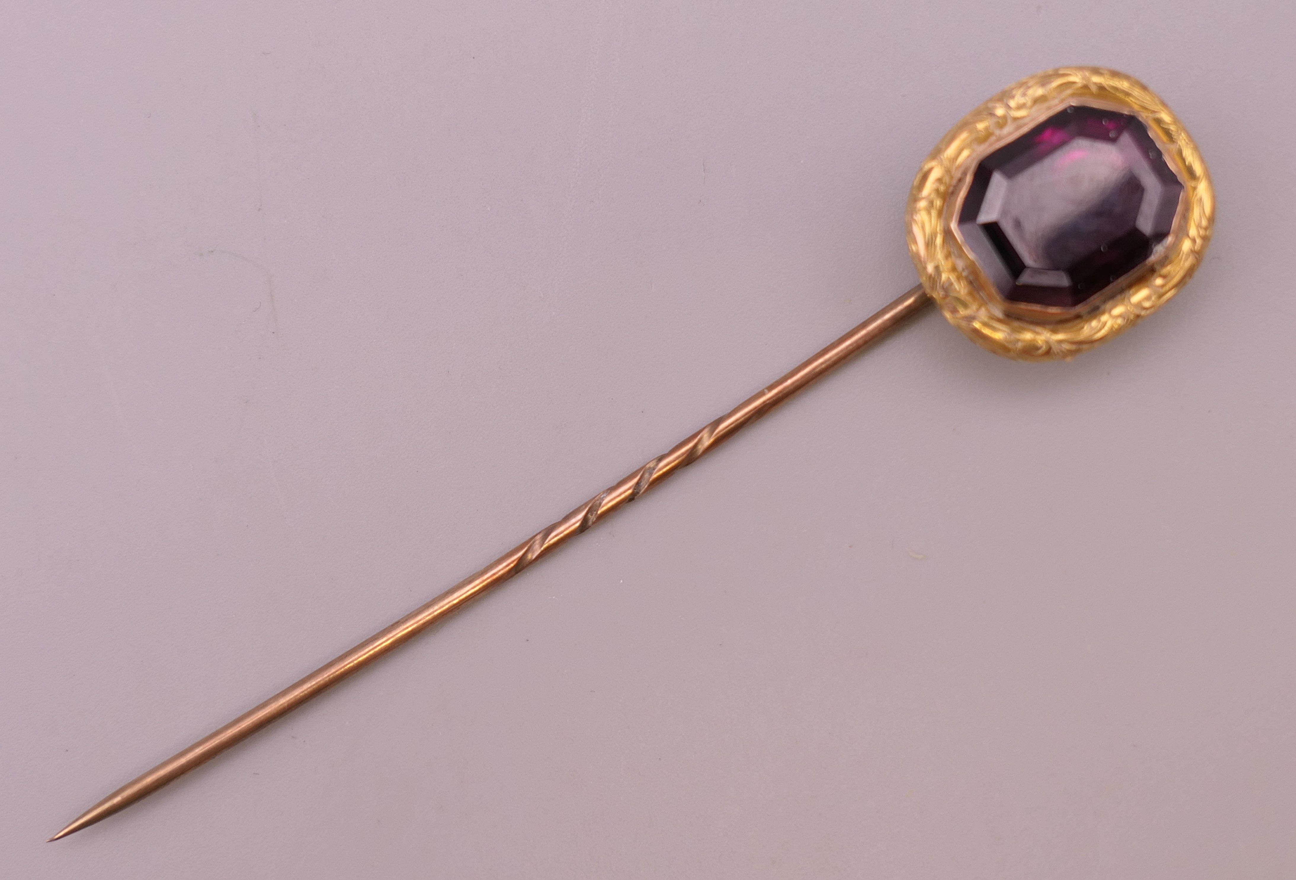An antique unmarked gold purple stone stickpin, possibly garnet, boxed. 8 cm high. 3.