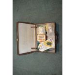 Brown leather case filled with fishing equipment including hook sharpeners, fishing glue, pliers,