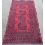 C20th traditional pattern wool rug, red ground with central field displaying four geometric