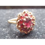 Hallmarked 9ct yellow gold garnet daisy cluster ring with a central round cut, claw set garnet and a