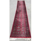 Red ground Bokhara pattern wool runner, field filled with elephant foot medallions, hooked medallion