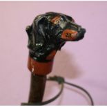 An ash shank walking stick with leather wrapped handle and thong and painted carved Daschund like