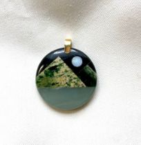 Green hardstone circular pendant with geometric pieces creating stylised landscape with opal moon,