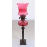 Early C20th oil lamp on burnished metal Corinthian column base with cranberry glass reservoir and