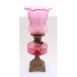 Early C20th oil lamp on moulded floral metal base with cranberry glass reservoir and etched