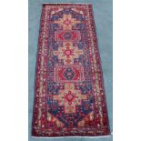 A Kordi woollen hand-made rug with red ground, 132 by 50ins. (335 by 127cms.).