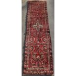 A Hamadan woollen hand-made runner with dark red ground, 151 by 38ins. (383 by 96cms.).