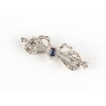 An unmarked white gold sapphire & diamond ribbon brooch, the cushion cut sapphire weighing