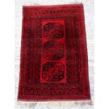 Property of a deceased estate - an Afghan hand knotted wool rug with three octagonal guls on a red