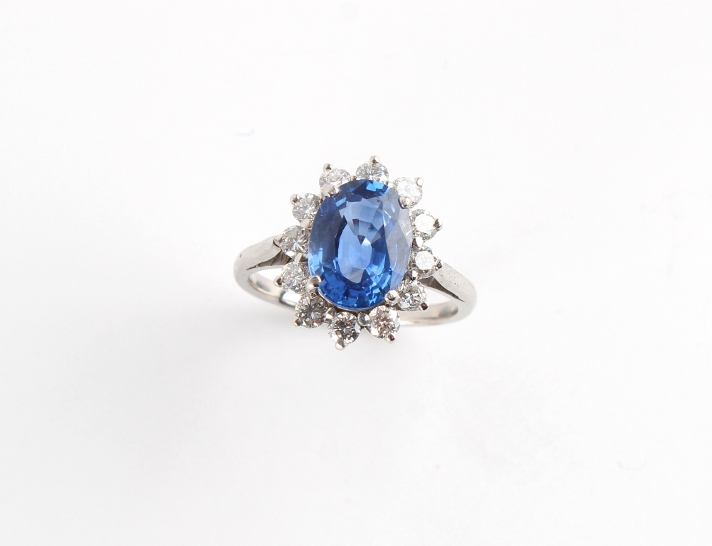 An unmarked white gold sapphire & diamond oval cluster ring, the oval cushion cut sapphire