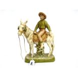 A Royal Dux Pottery Model of a Boy Riding a Donkey, on a rocky oval base, in typical muted tones
