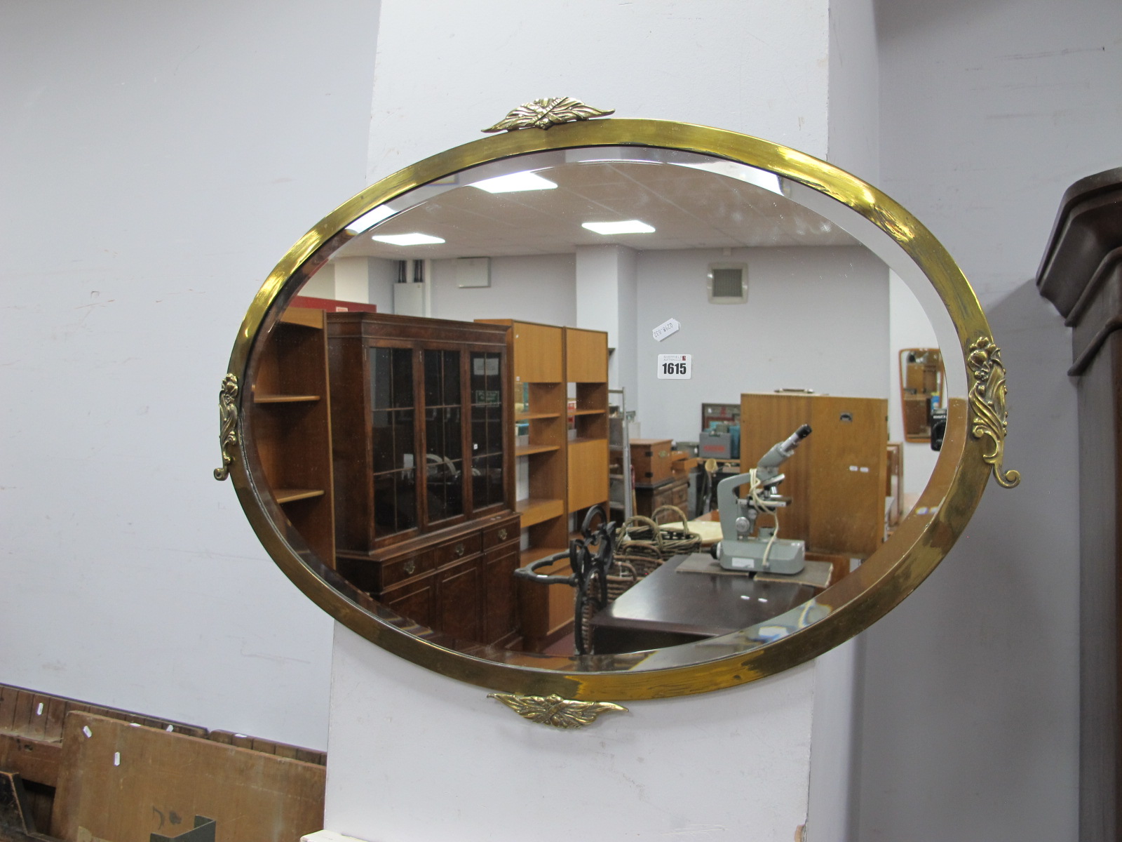 An Early XX Century Oval Bevelled Wall Mirror, in brass frame, with scroll mounts, 82cm wide.