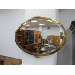 An Early XX Century Oval Bevelled Wall Mirror, in brass frame, with scroll mounts, 82cm wide.