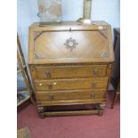 A 1920's Oak Bureau, with fall font fitted interior, three long drawers, on cup-cover supports,